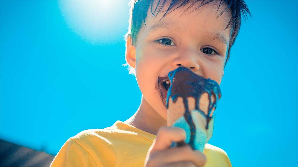 young boy with a yellow shirt eating blue ice cream on a sunny day